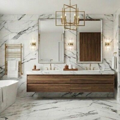 Bathroom with floating wood vanity, marble tile, large mirrors, and gold fixtures.
