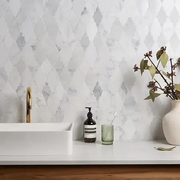 Bathroom with white diamond-patterned marble tile wall, white sink, gold faucet, and decorative items.
