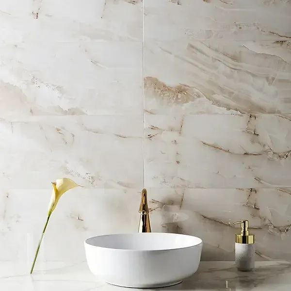White bathroom with marble tiles, a round sink, gold faucet and dispenser, and a yellow flower.