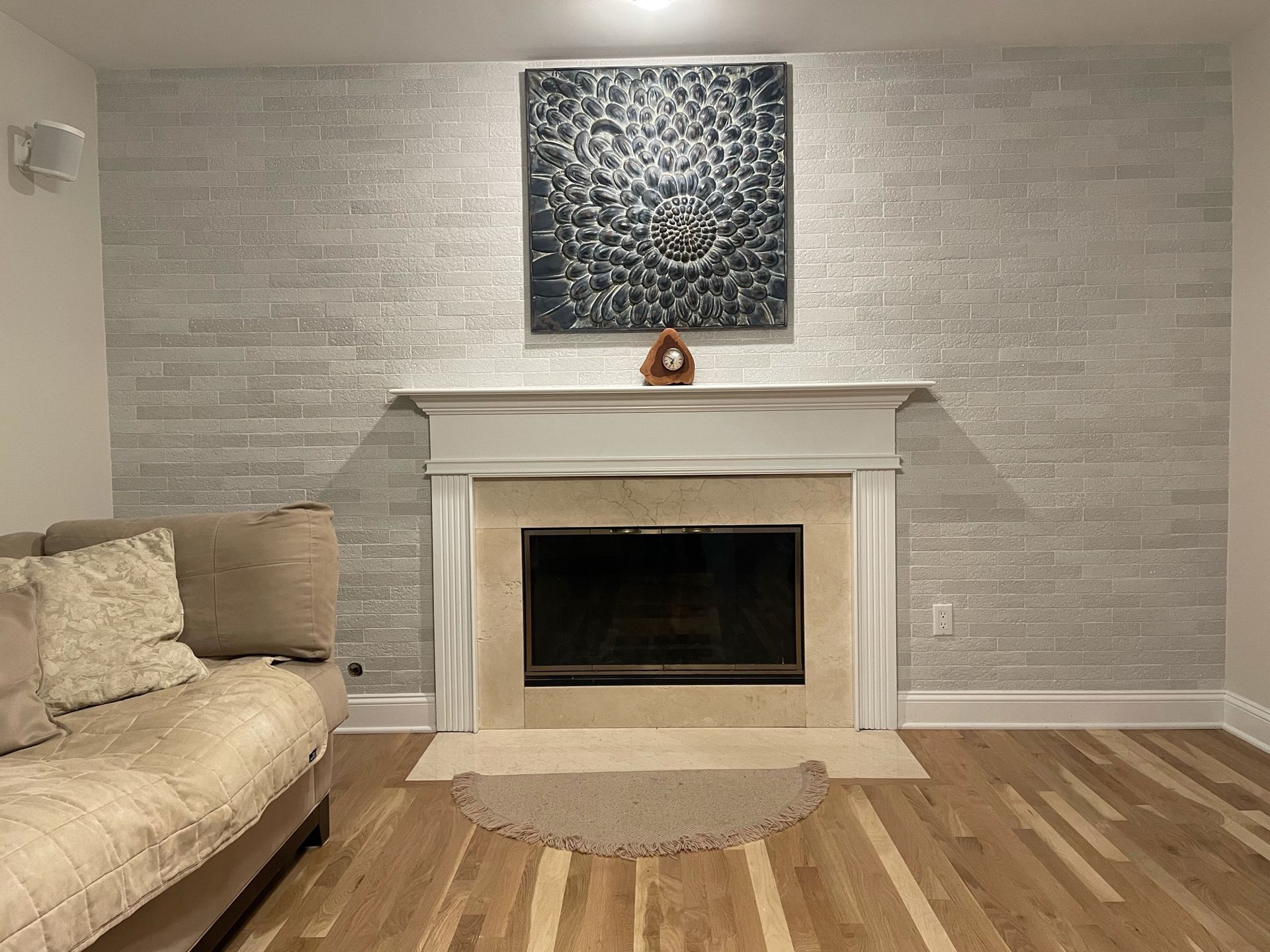 Living room with beige sofa and white fireplace on gray wall, patterned art above and wood floor.