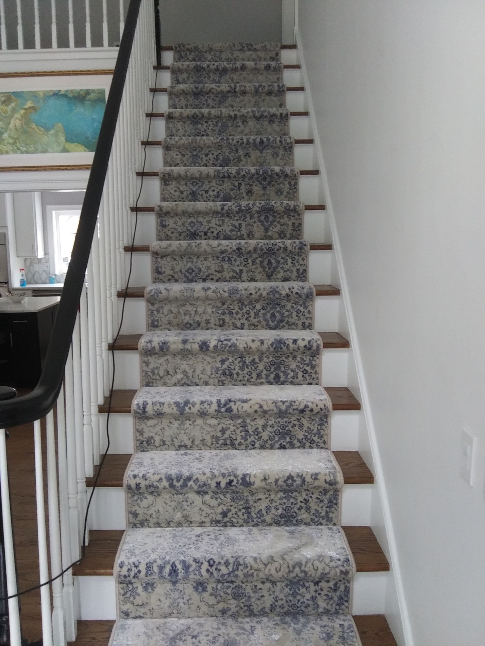 Carpeted staircase with patterned runner and white walls, viewed from the bottom.