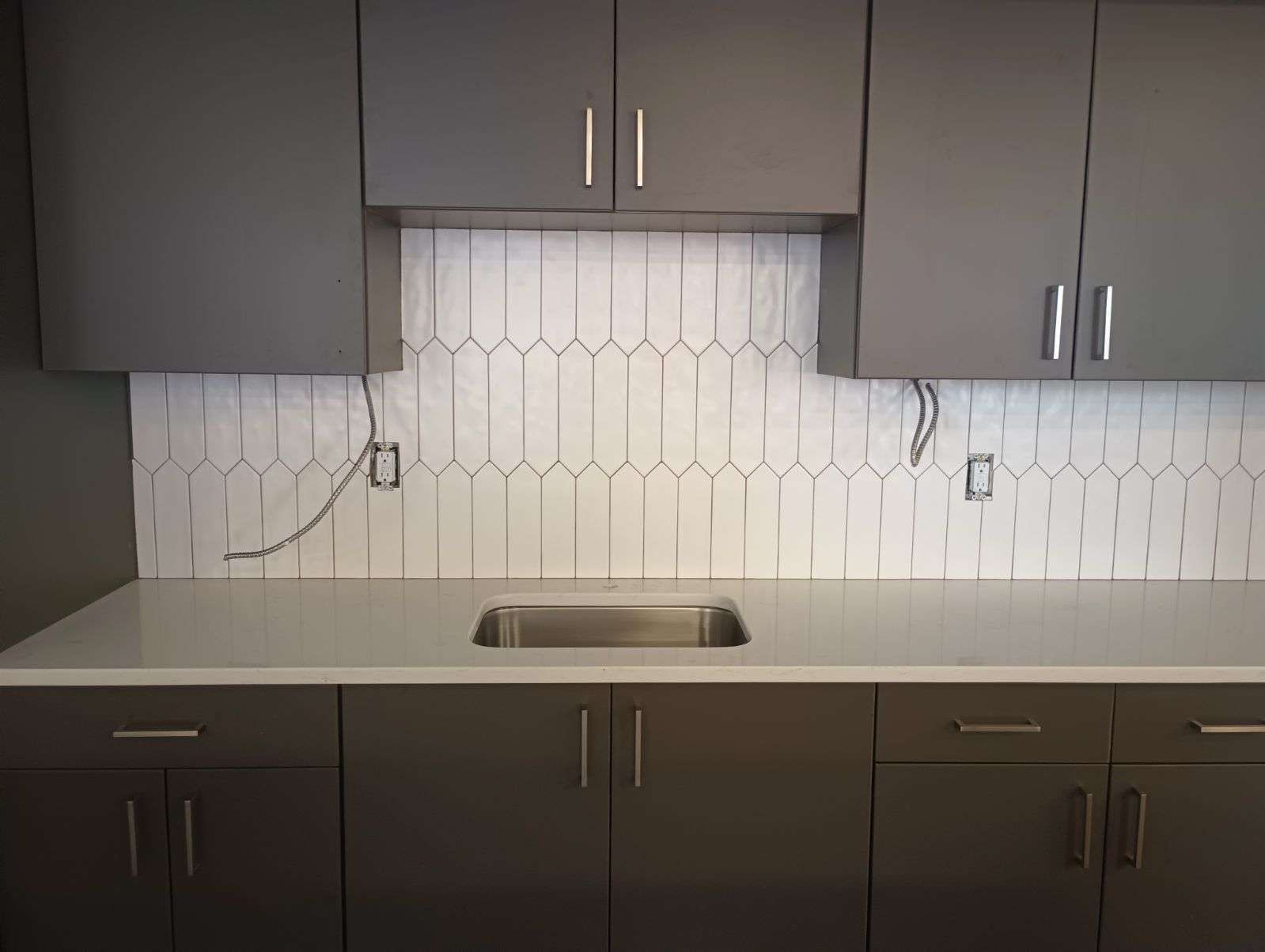 Modern kitchen with dark cabinets, white backsplash, and a sink centered beneath upper cabinets.