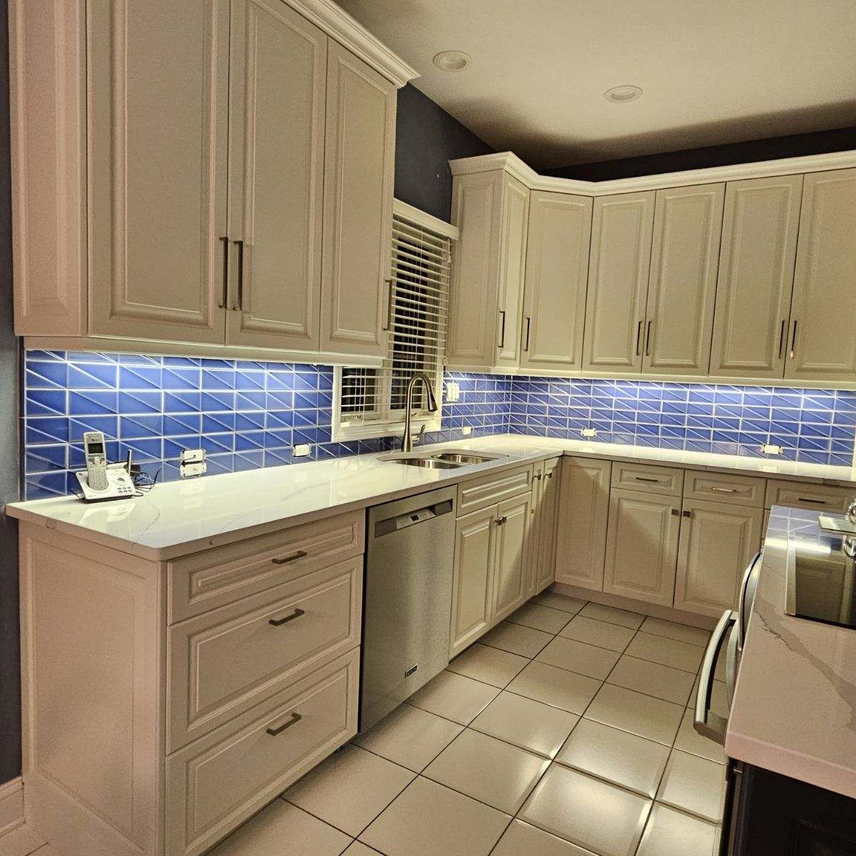 Bright kitchen with beige cabinets, blue tile backsplash, white countertops, and tiled floor.