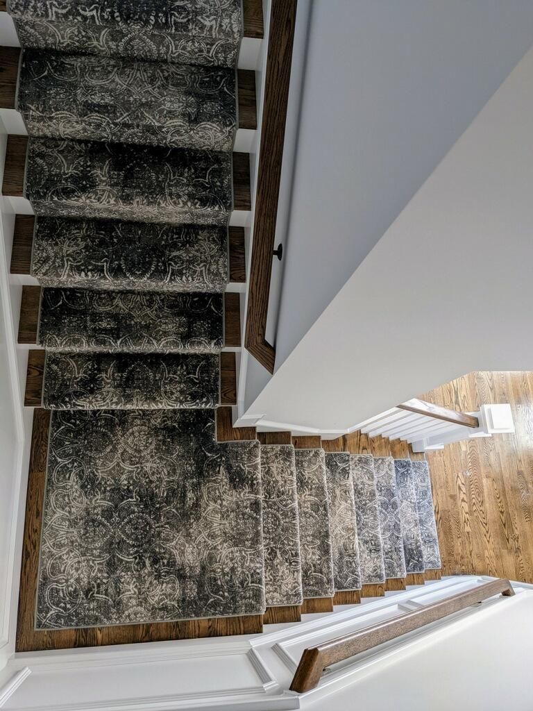 Top-down view of carpeted stairs with a white railing and wood trim in a bright stairwell
