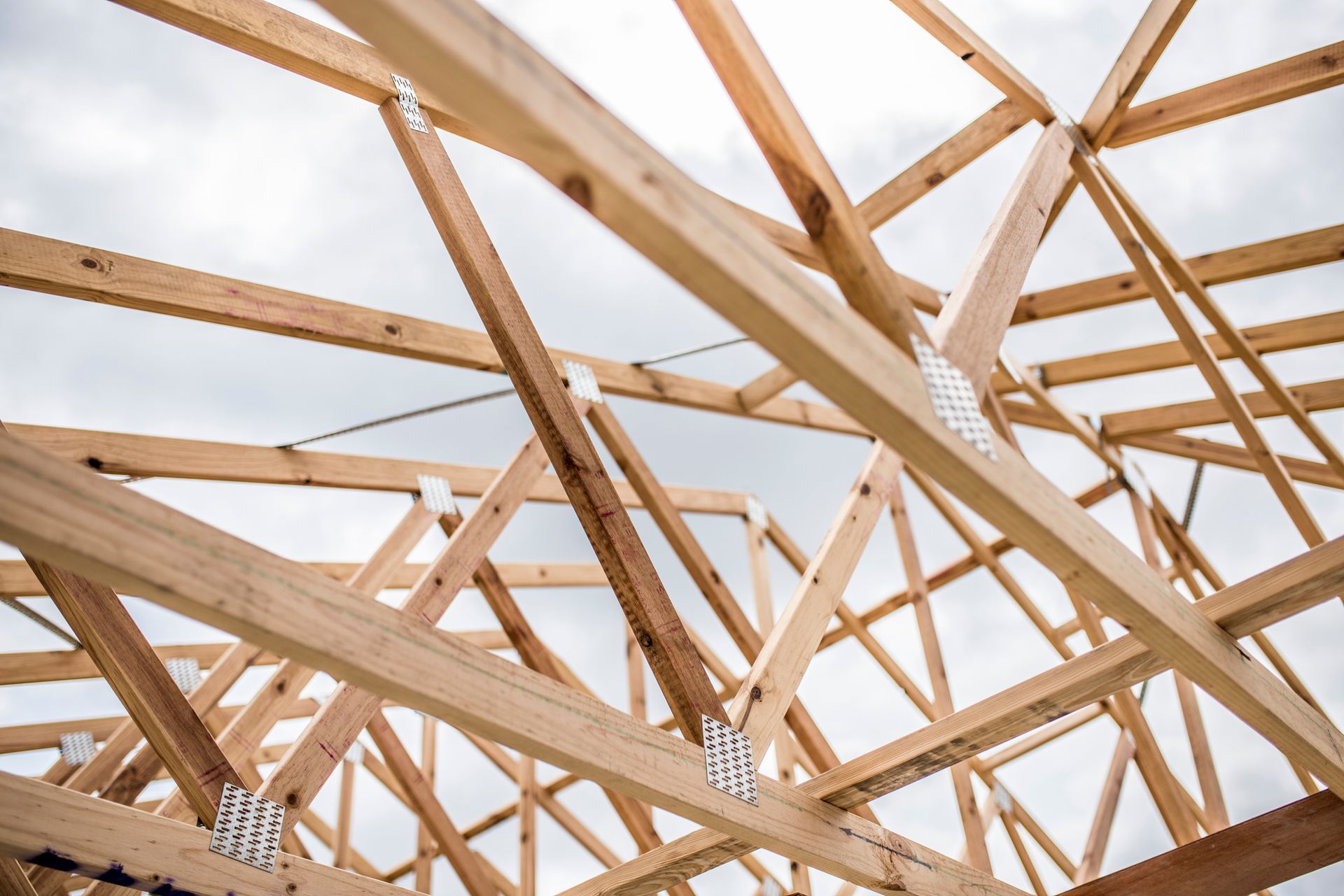 Wooden roof trusses under construction against a cloudy sky.