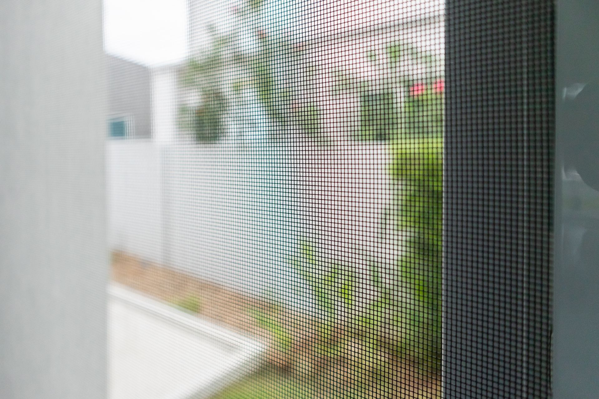 View through a window screen of a garden path and greenery beside a building
