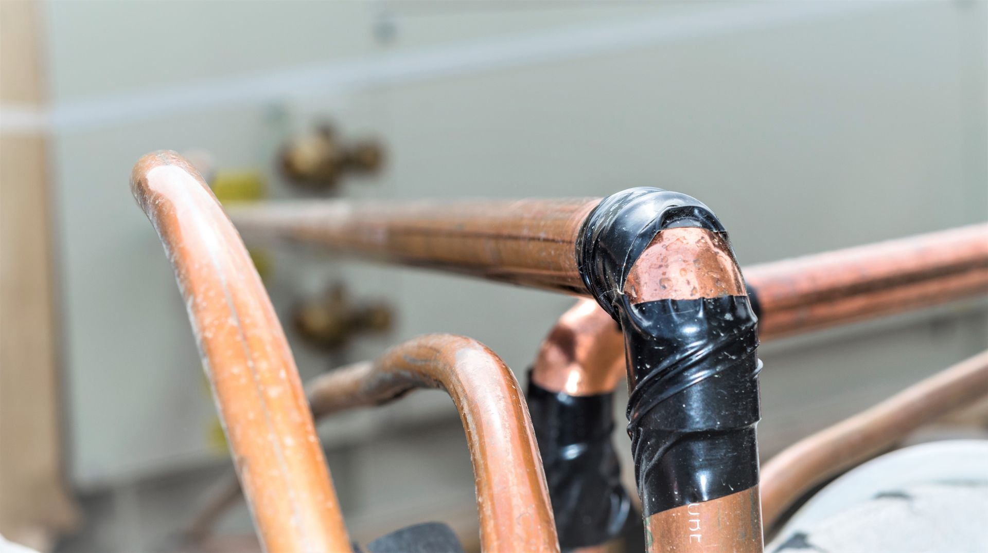 Copper pipes with black tape at a bend, possibly leaking. Water vapor visible; background shows equipment.