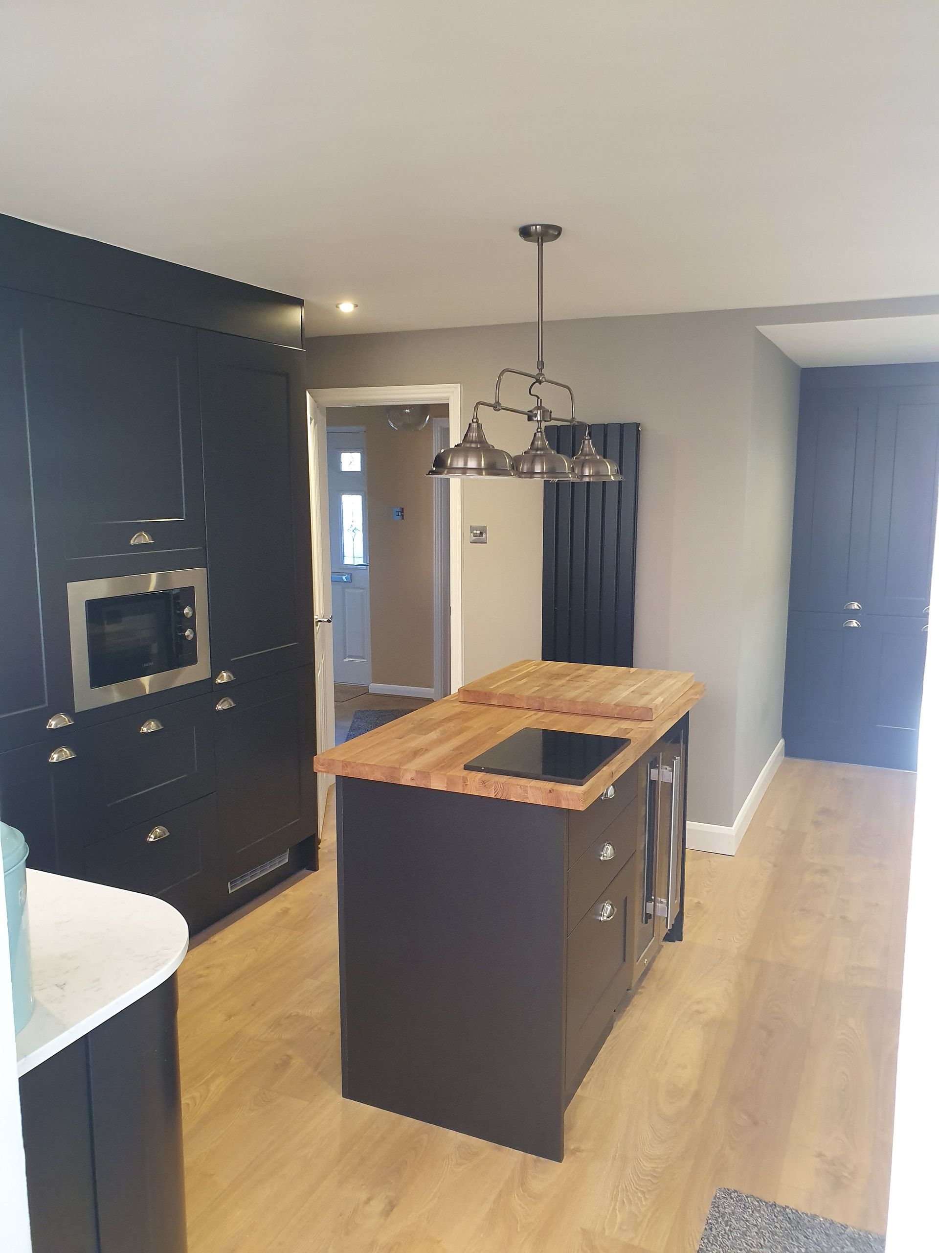 New kitchen with dark grey cupboards and stone worktops with central island and oak worktop, island pendant and wine fridge and a designer dark grey radiator in the background