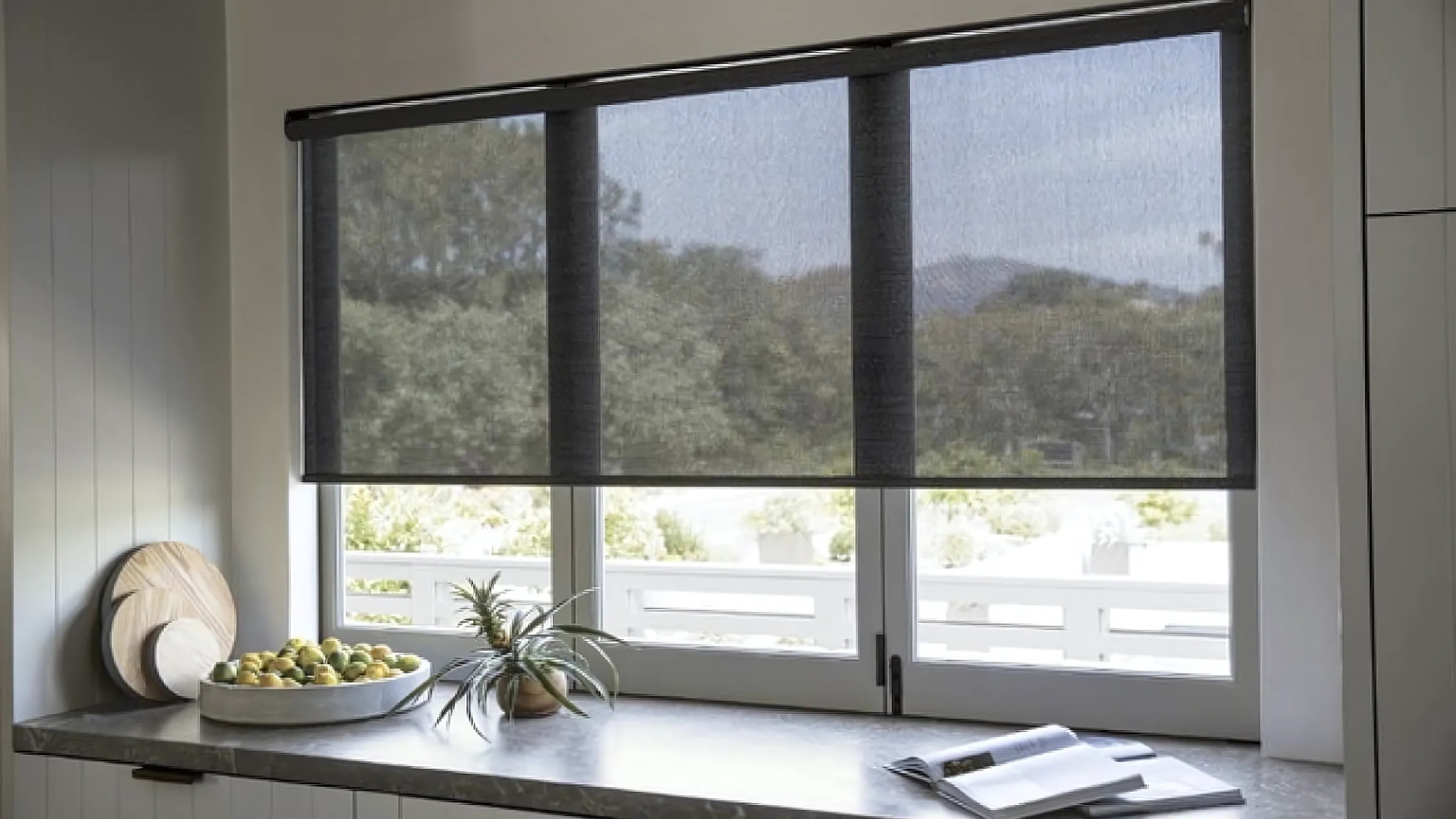 Motorized blackout roller shades – master bedroom – Rancho Cucamonga
A kitchen window with black blinds and a bowl of fruit on the counter.