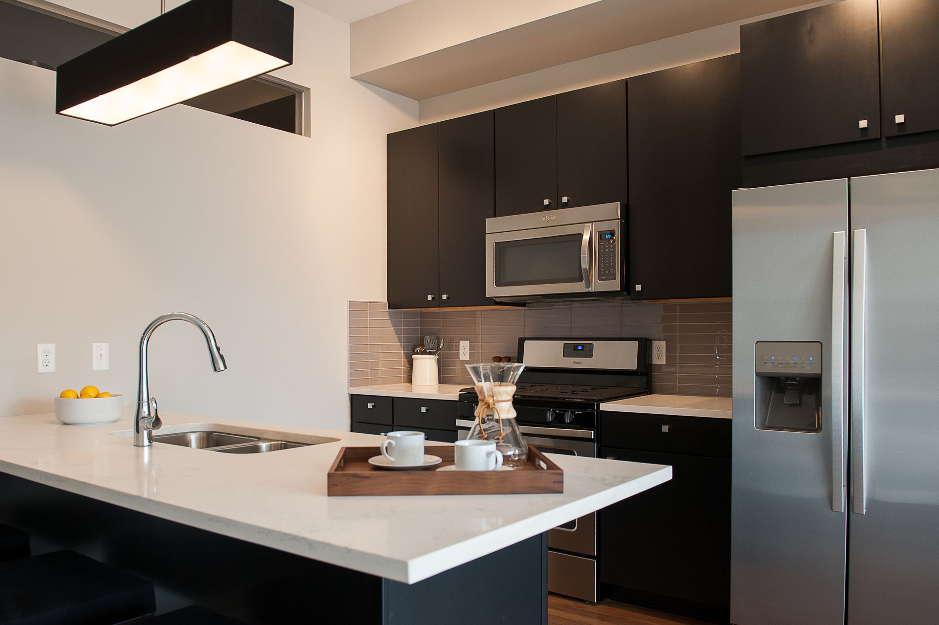 A kitchen with black cabinets , a stainless steel refrigerator , a microwave , and a sink.