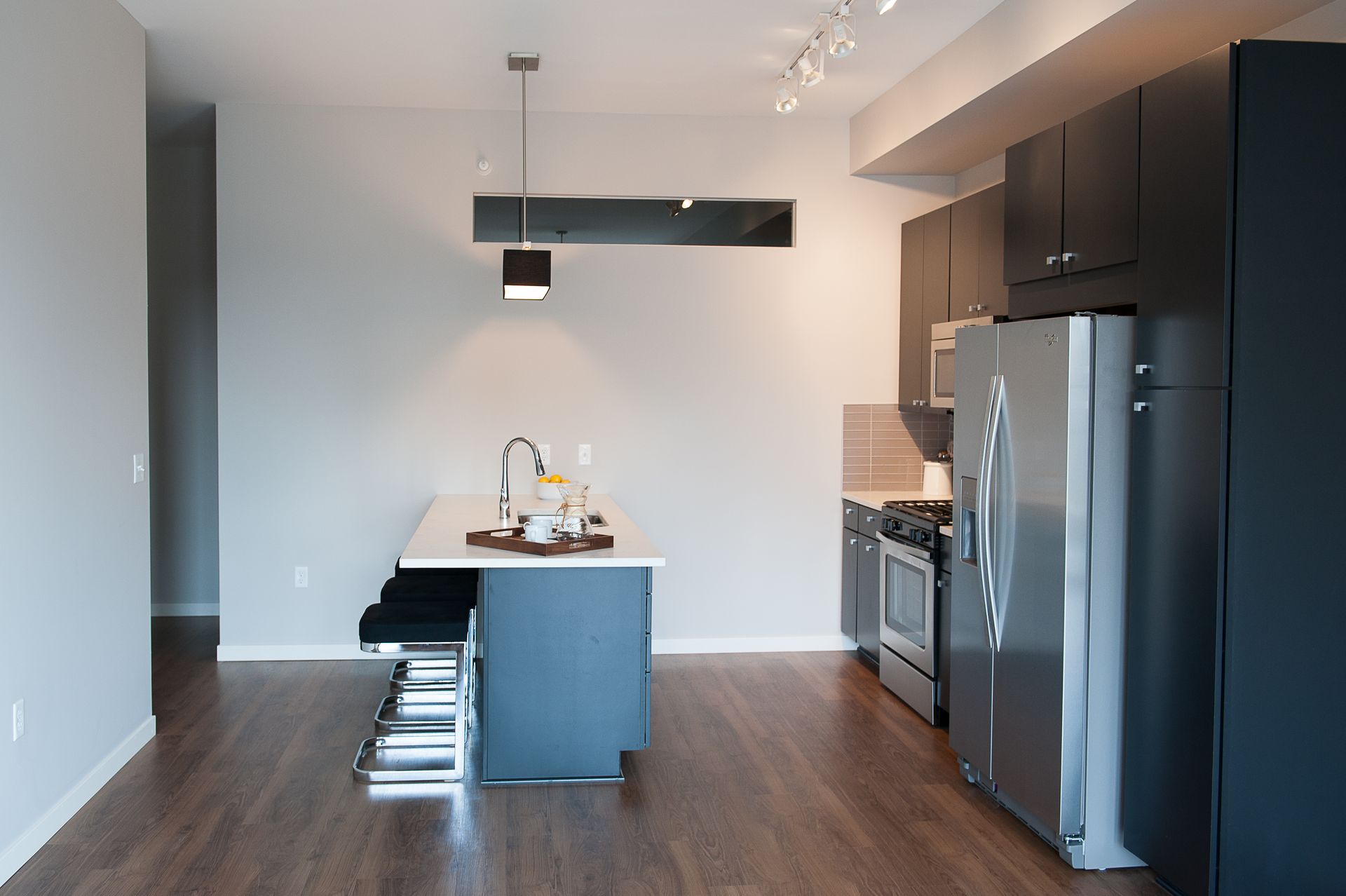 A kitchen with black cabinets and a stainless steel refrigerator