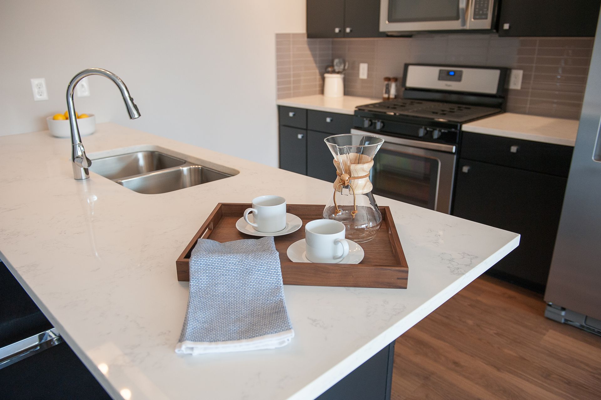 A kitchen with a sink , stove , microwave and a tray on the counter.