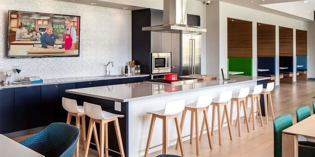 Modern kitchen with large island, bar stools, and TV showing cooking show.