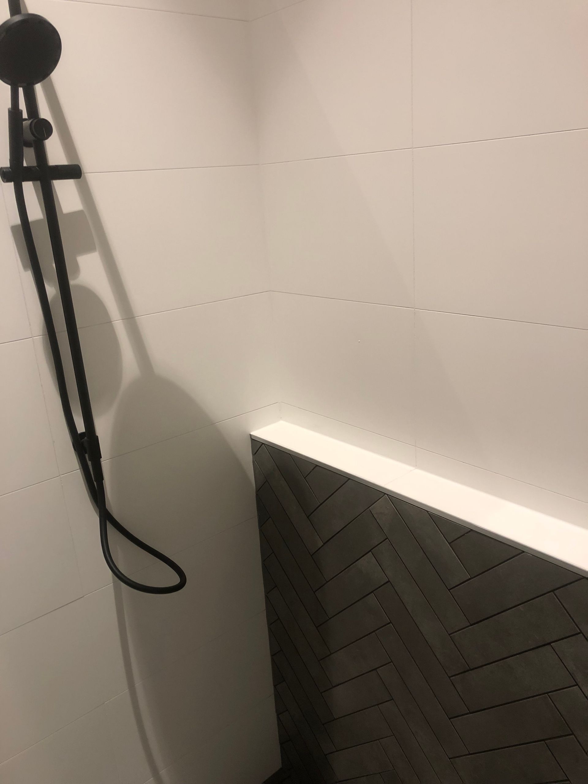 A black shower head is hanging from a white wall in a bathroom.