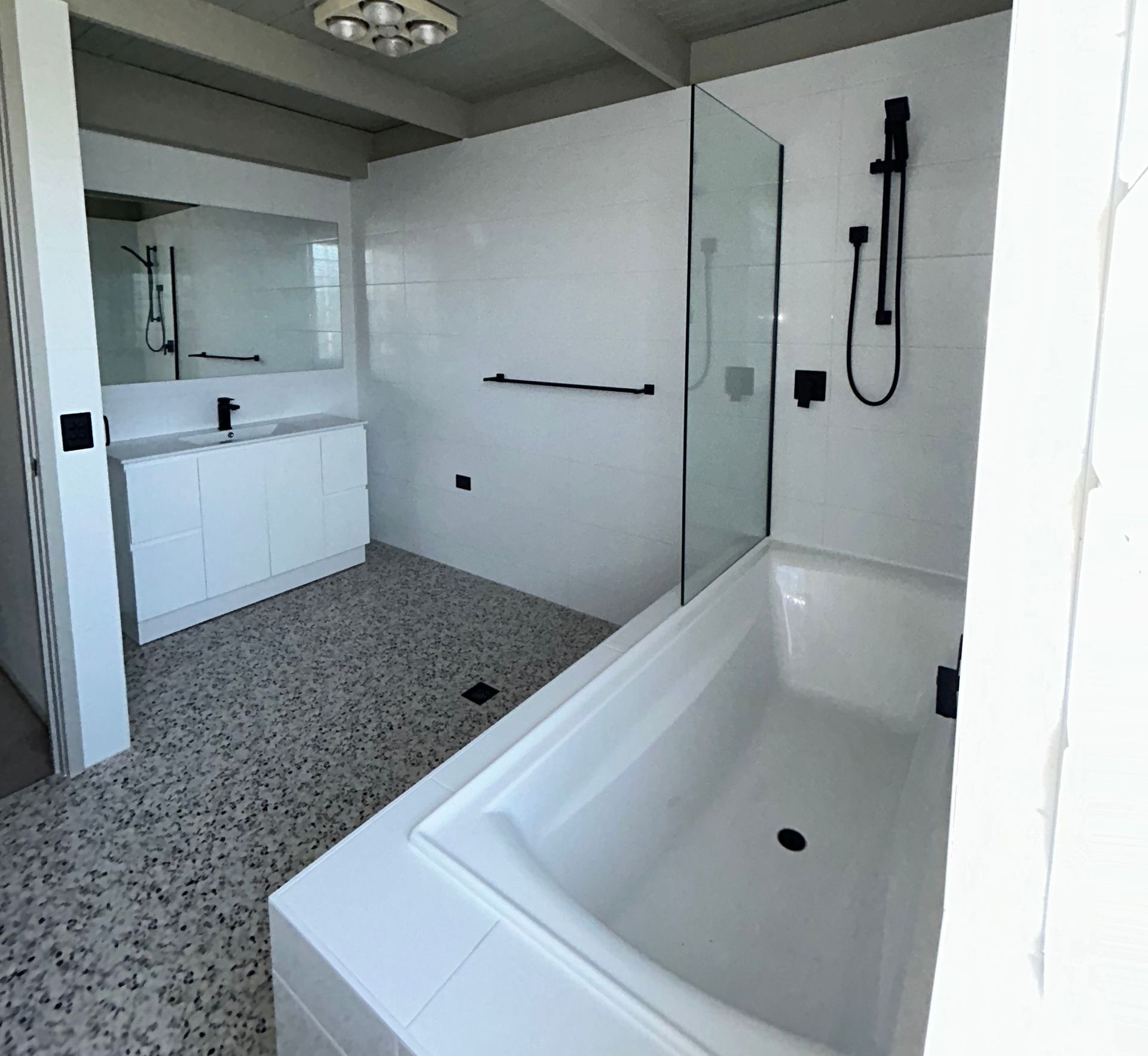 Modern white bathroom with tub, shower, vanity, black fixtures, and speckled flooring.