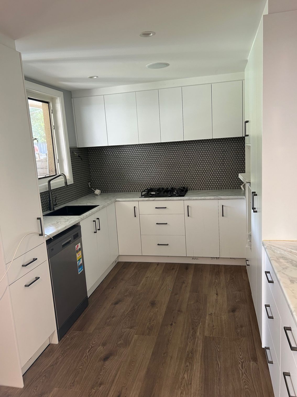 White kitchen with wooden floors, black backsplash, and appliances.