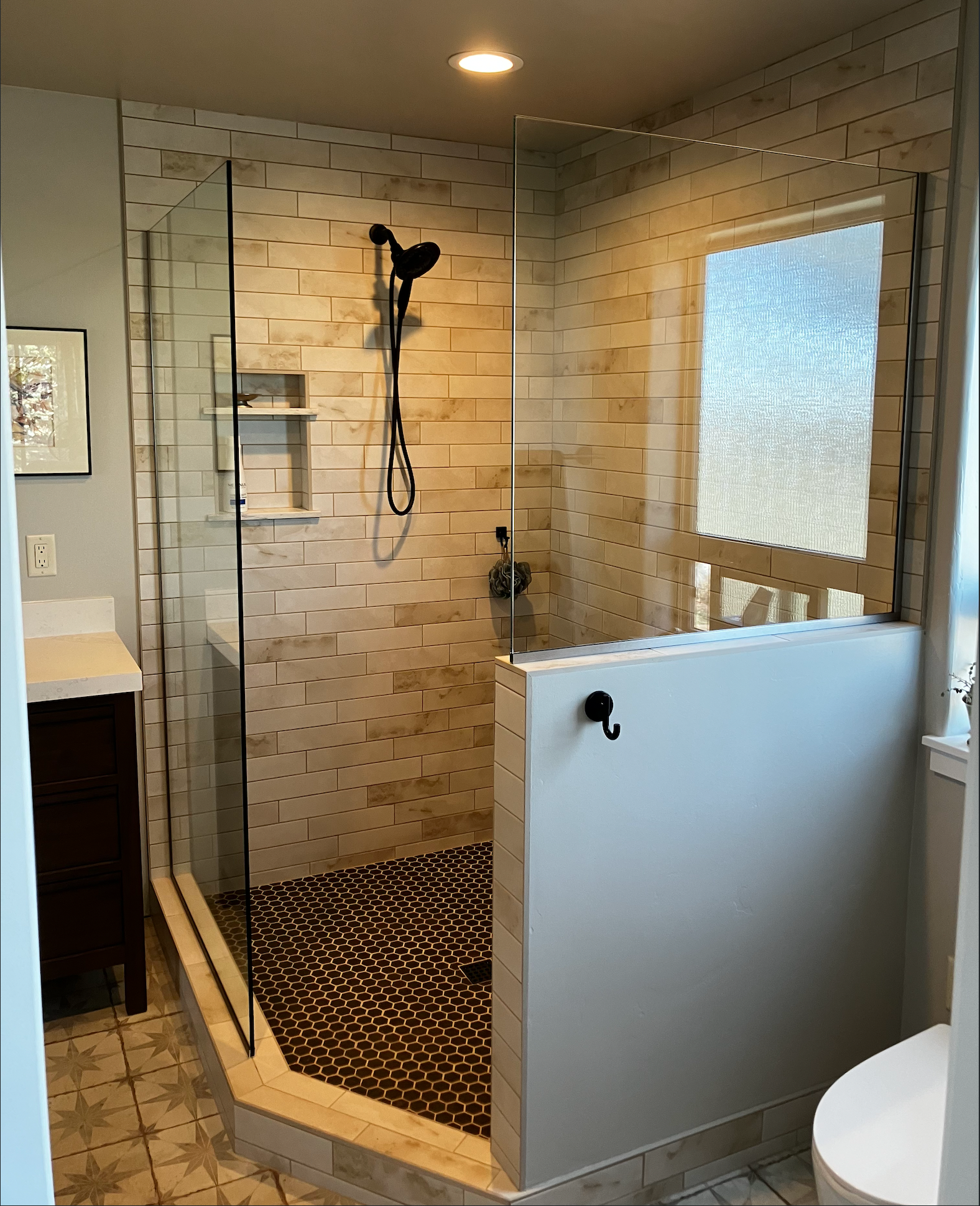A walk-in shower with stone-tiled walls, glass panels, a patterned floor, and a half-wall partition in a modern bathroom.