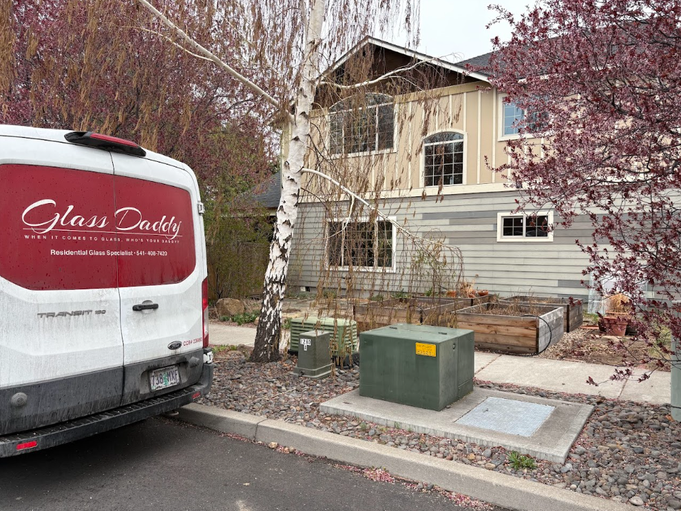 Residential driveway with a white van, birch tree, utility boxes, and a two-story house in fall.
