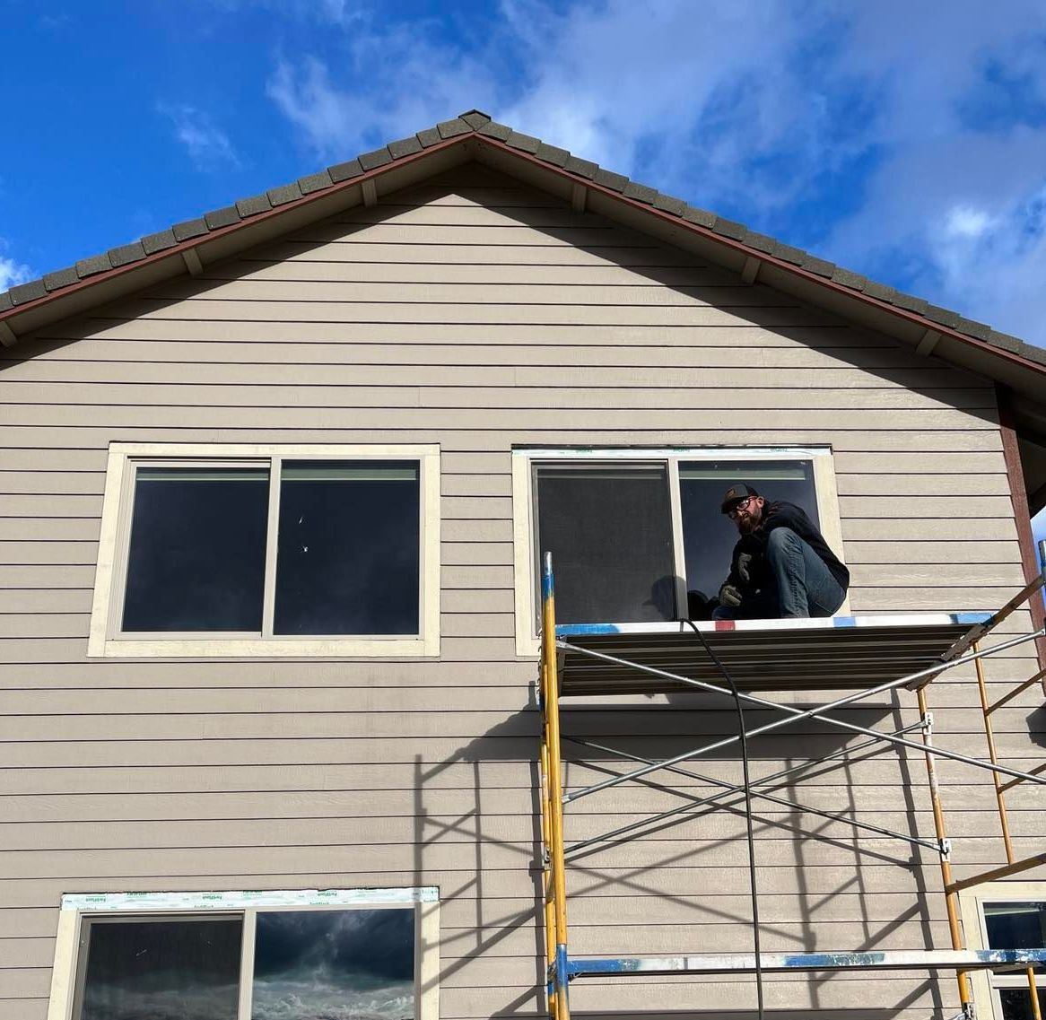 A man sits on a scaffolding on the side of a house