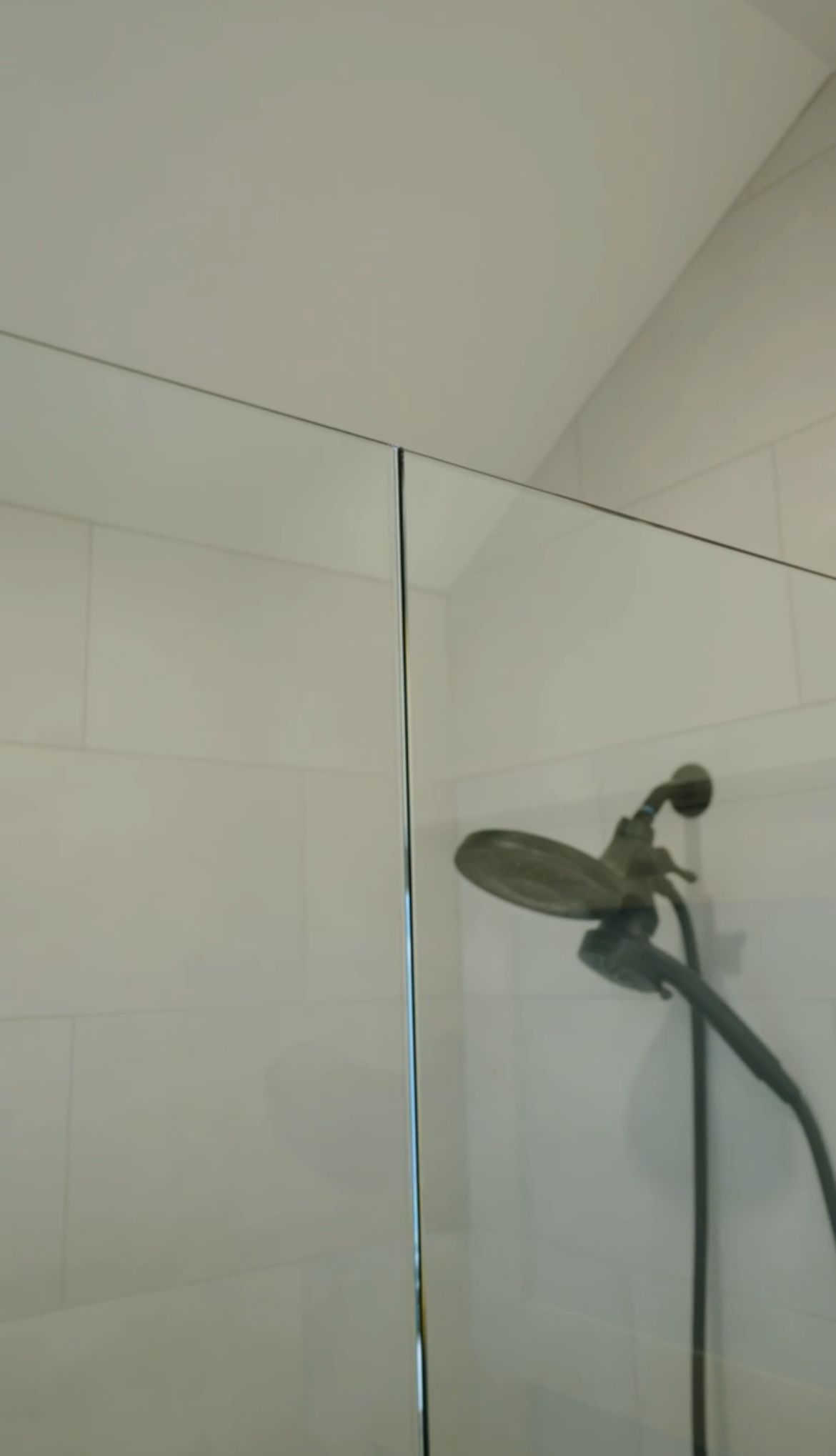 Showerhead mounted on a glass shower wall in a tiled bathroom