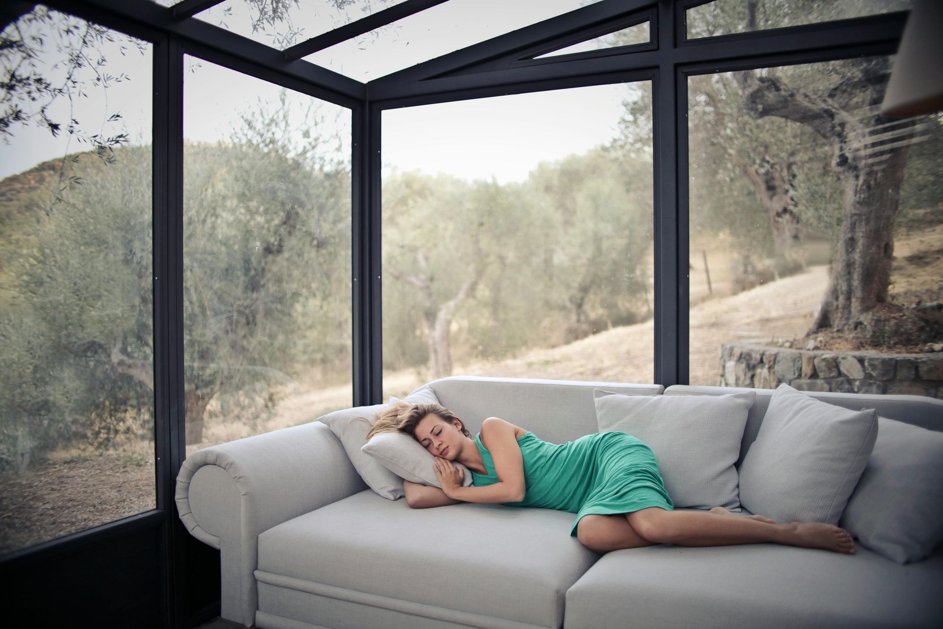 A woman in a green dress is sleeping on a couch in a conservatory.