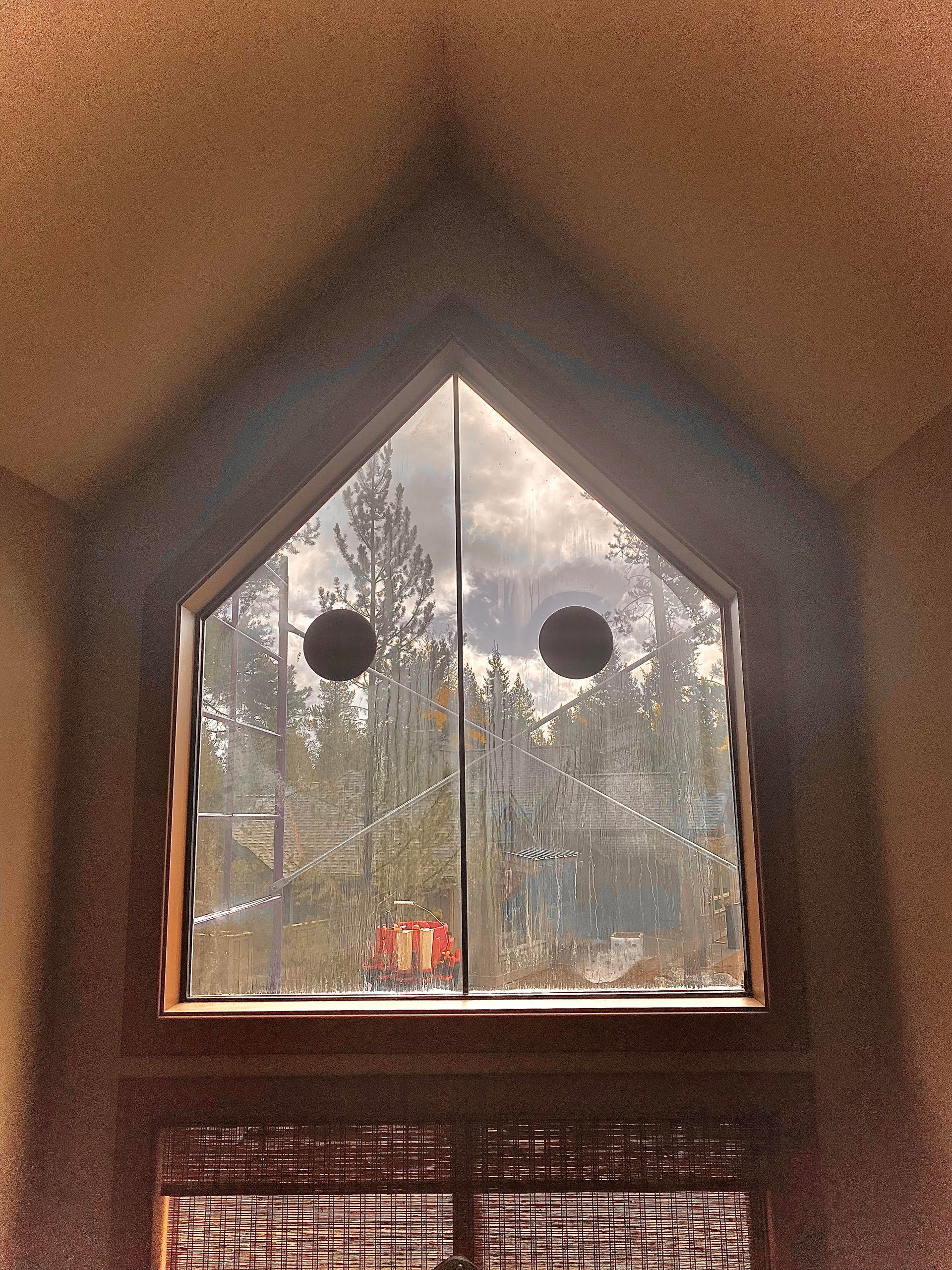 A triangle shaped window with a reflection of trees in it