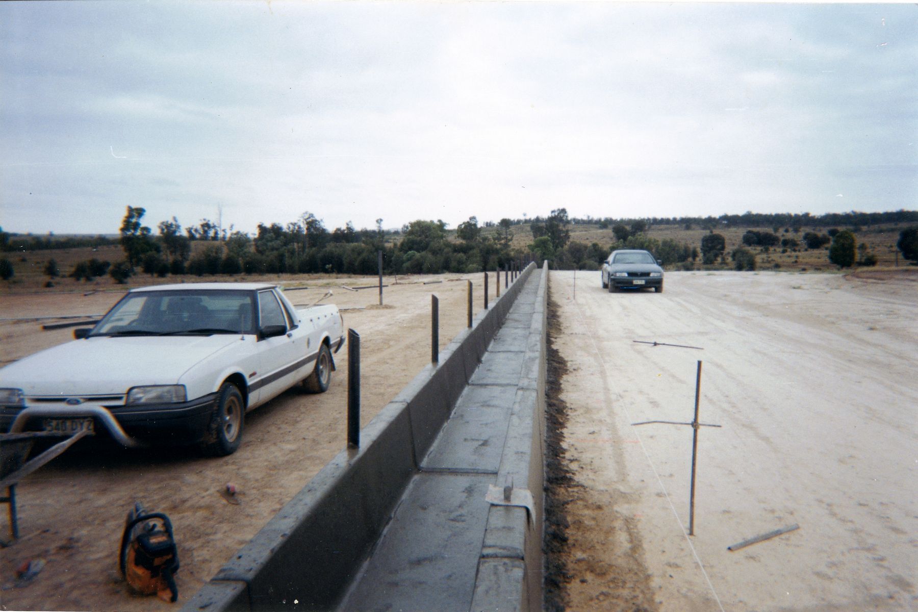 A white car is parked on the side of a dirt road