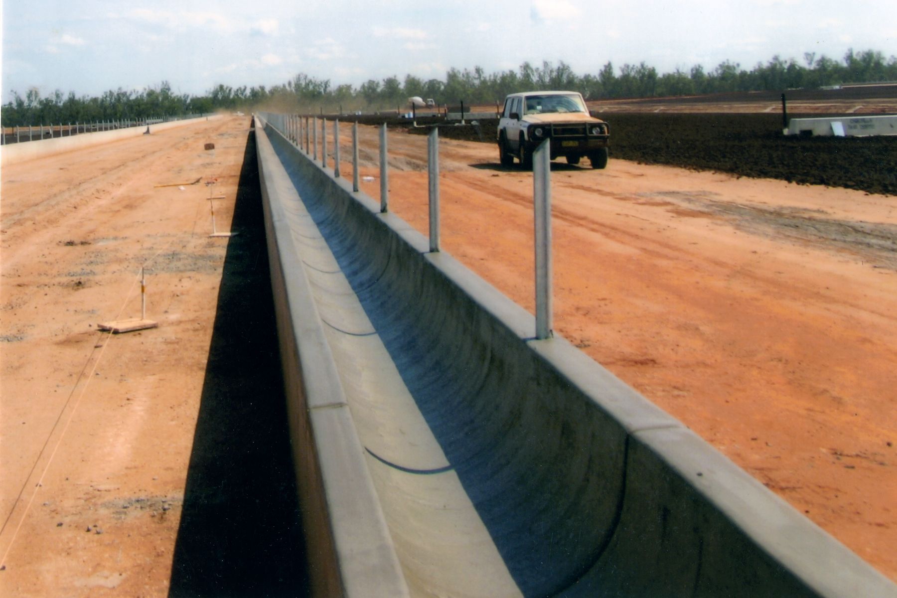 A truck is driving down a dirt road next to a concrete barrier