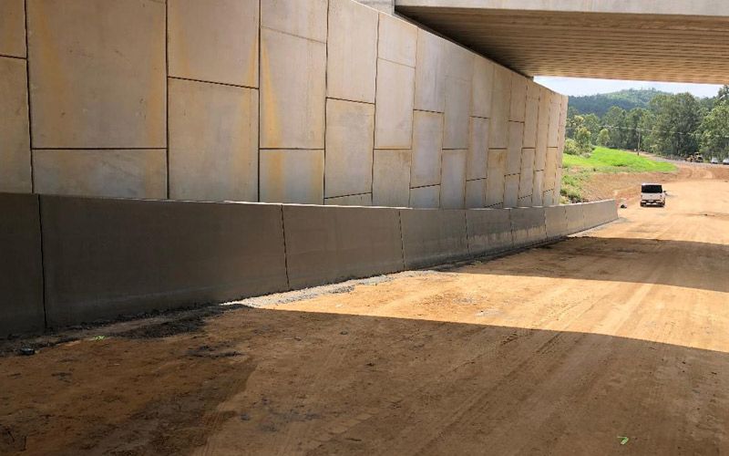 A car is driving under a bridge over a dirt road.