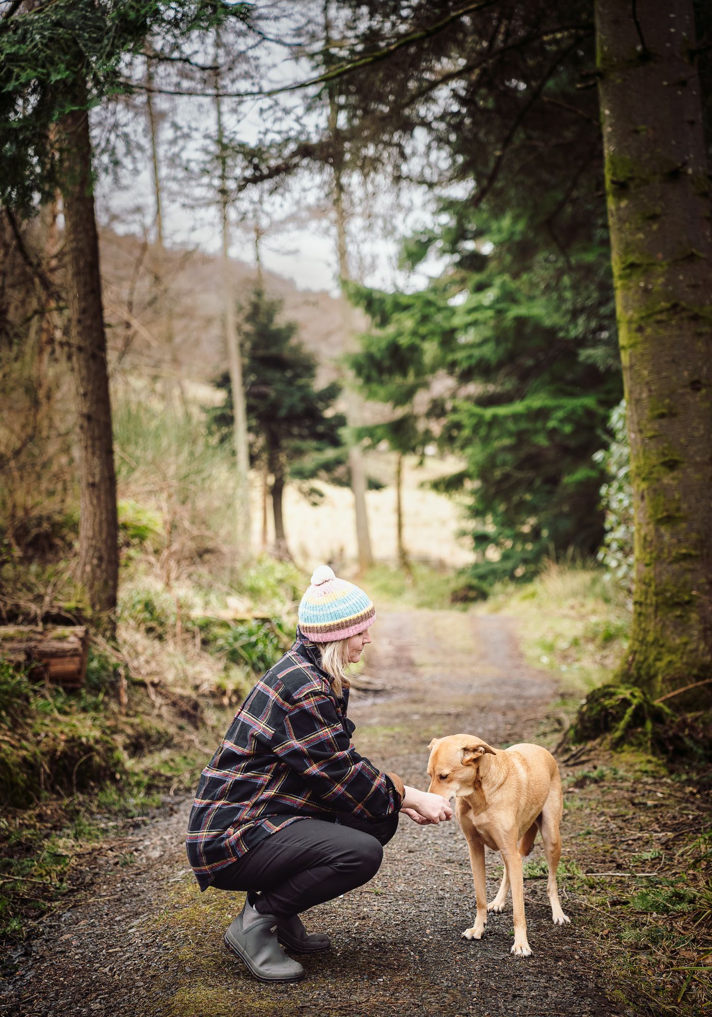 woman in forest kneeling beside yellow dog