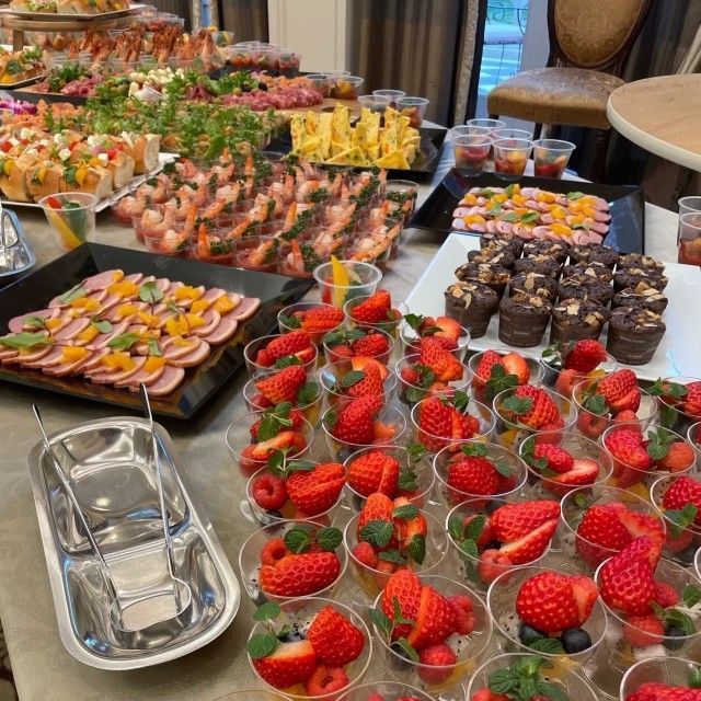 Buffet table with various appetizers and desserts, including sushi, fruit, and mini chocolate cakes.