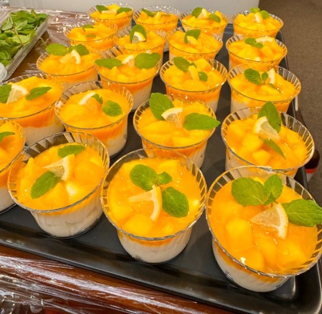 Mango sticky rice desserts in clear cups, garnished with mint and lemon slices.