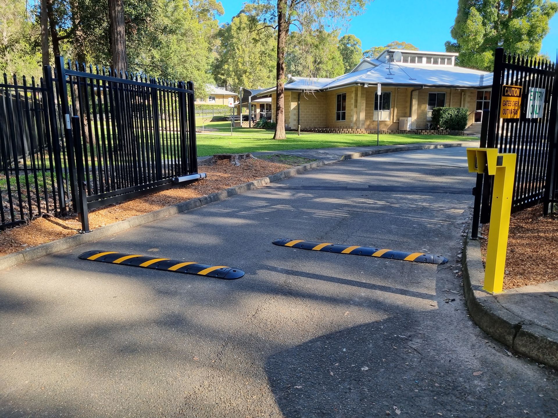 Open Black Gate With Speed Bumps, Leading to a Building — Strike Fencing & Gates In Tuggerah, NSW