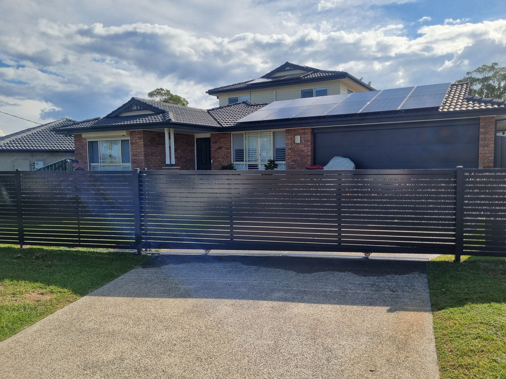 Black Metal Security Fence Along a Sidewalk, With a Building — Strike Fencing & Gates In Tuggerah, NSW