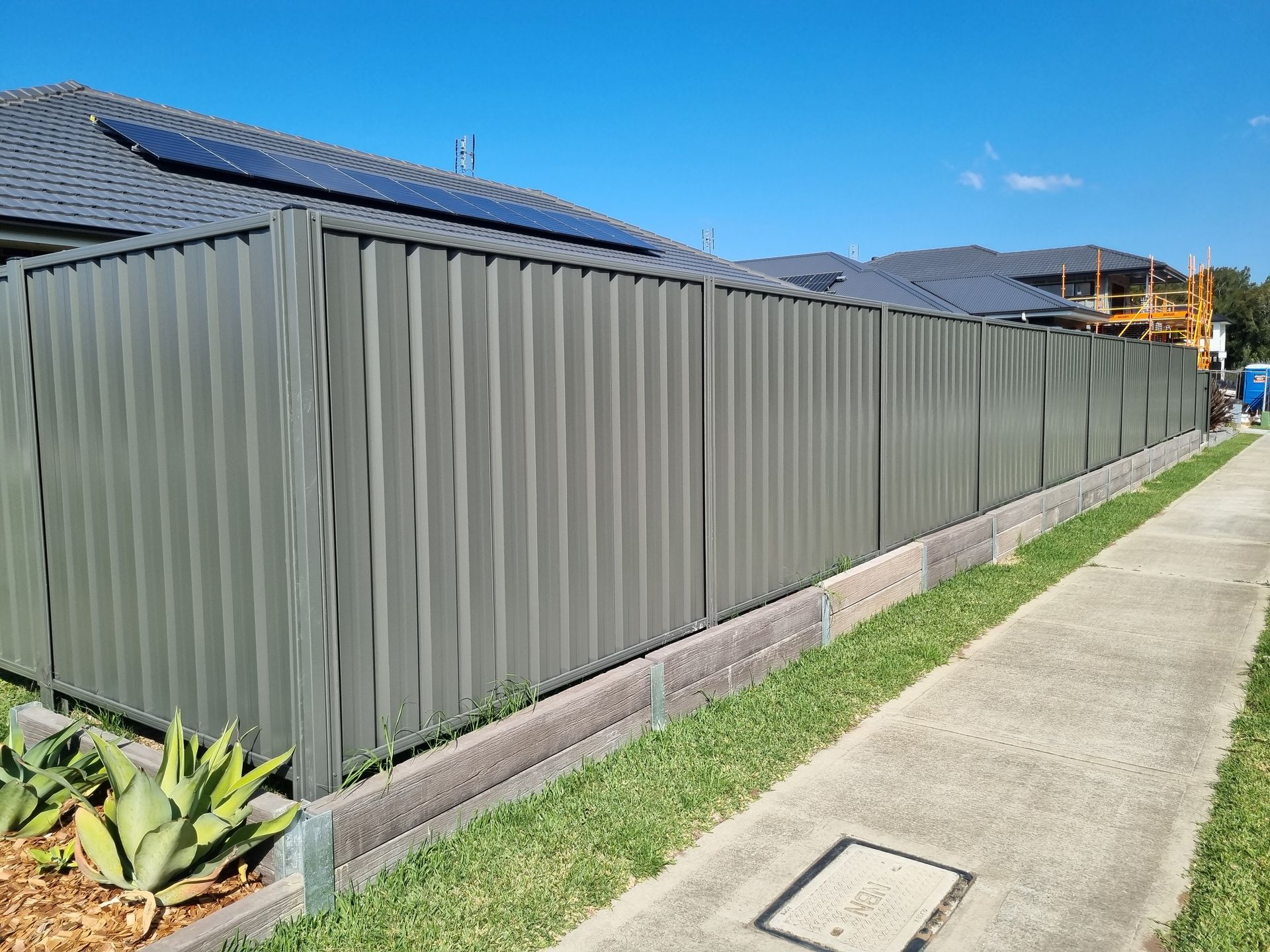 Green corrugated metal fence along a sidewalk with blue sky in the background. — Strike Fencing & Gates In Tuggerah, NSW