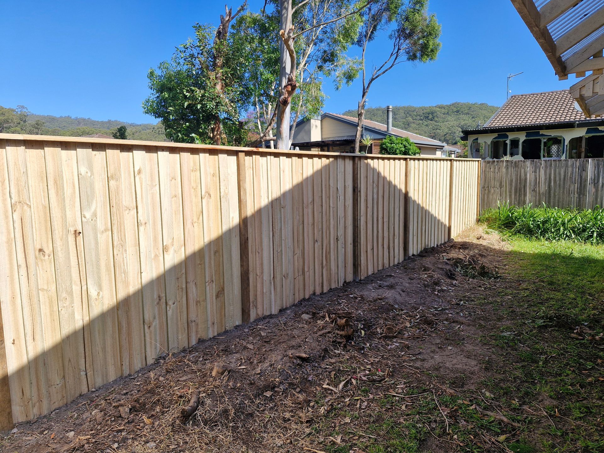 Timber fencing with the shade of the house covering half of the fence in front of a patch of grass