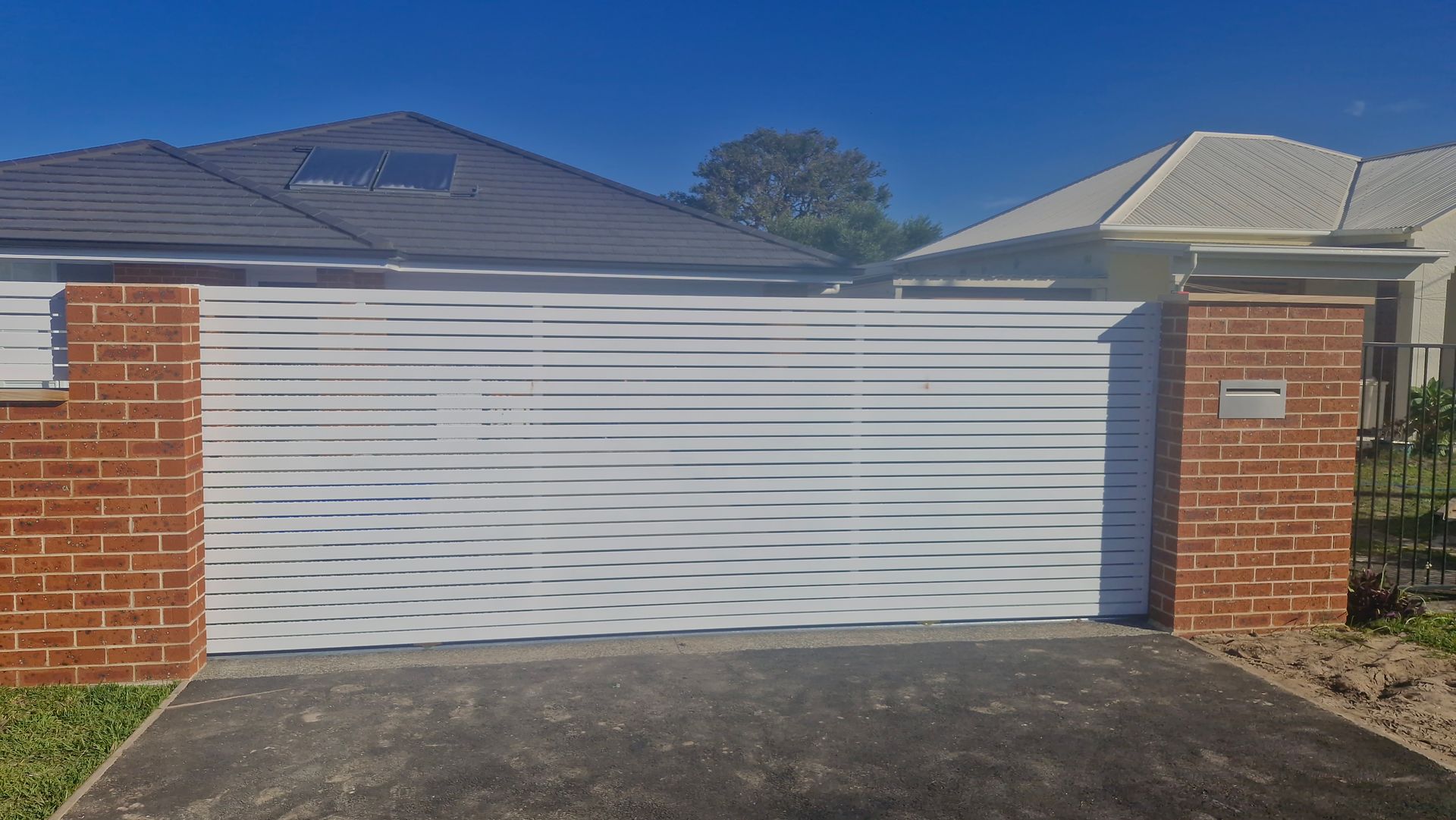 White horizontal slat gate between brick pillars; driveway entrance. — Strike Fencing & Gates In Tuggerah, NSW
