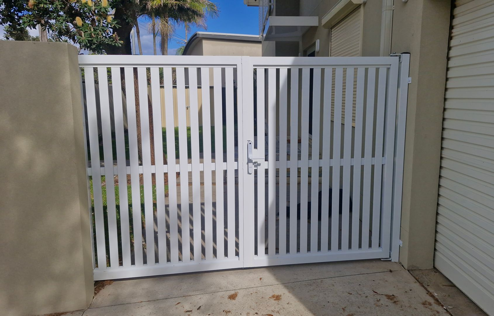 White metal double gate with vertical bars, blocking a driveway. — Strike Fencing & Gates In Tuggerah, NSW