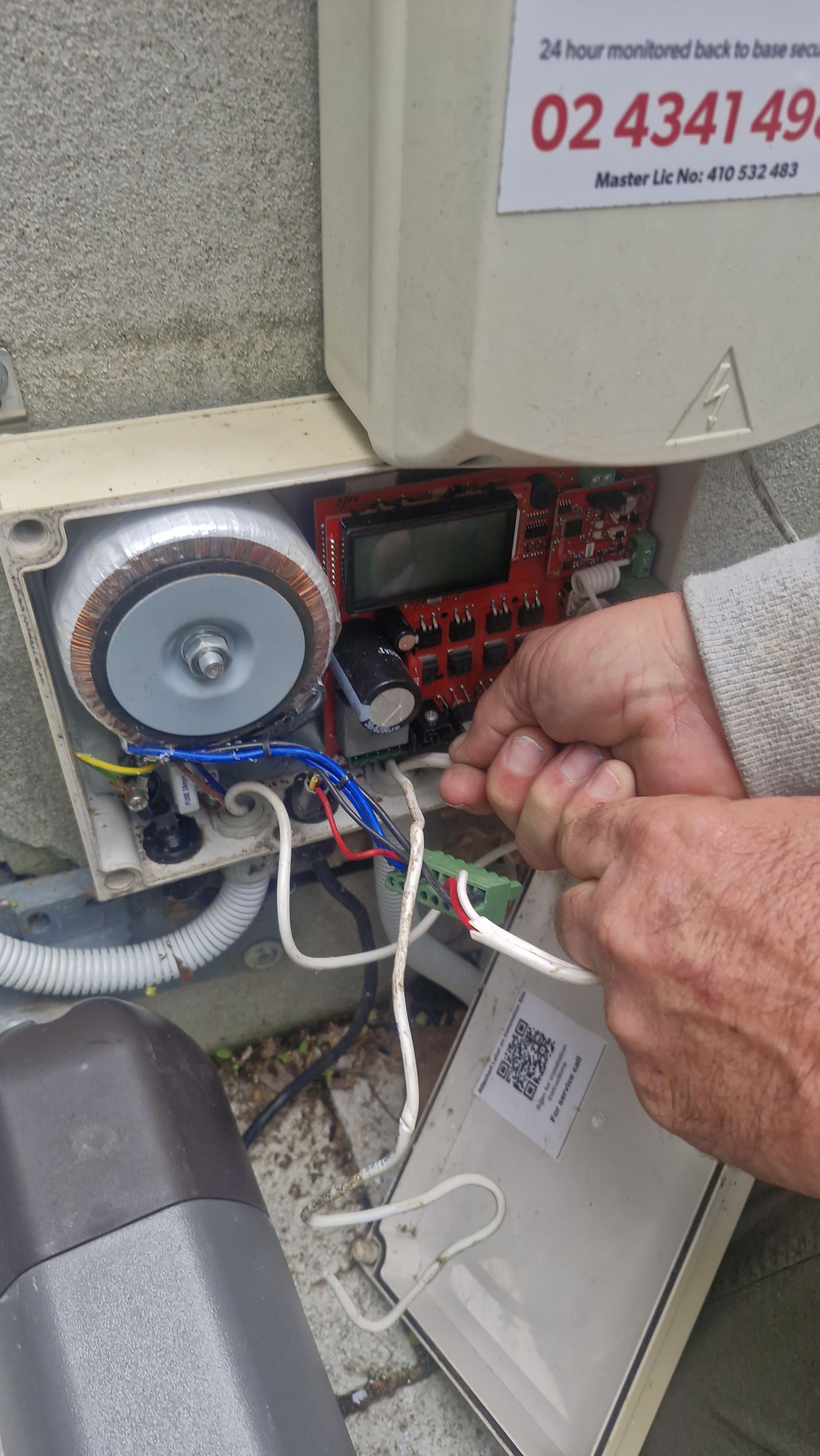 Person wiring an electrical box, with exposed circuits and transformer. — Strike Fencing & Gates In Tuggerah, NSW