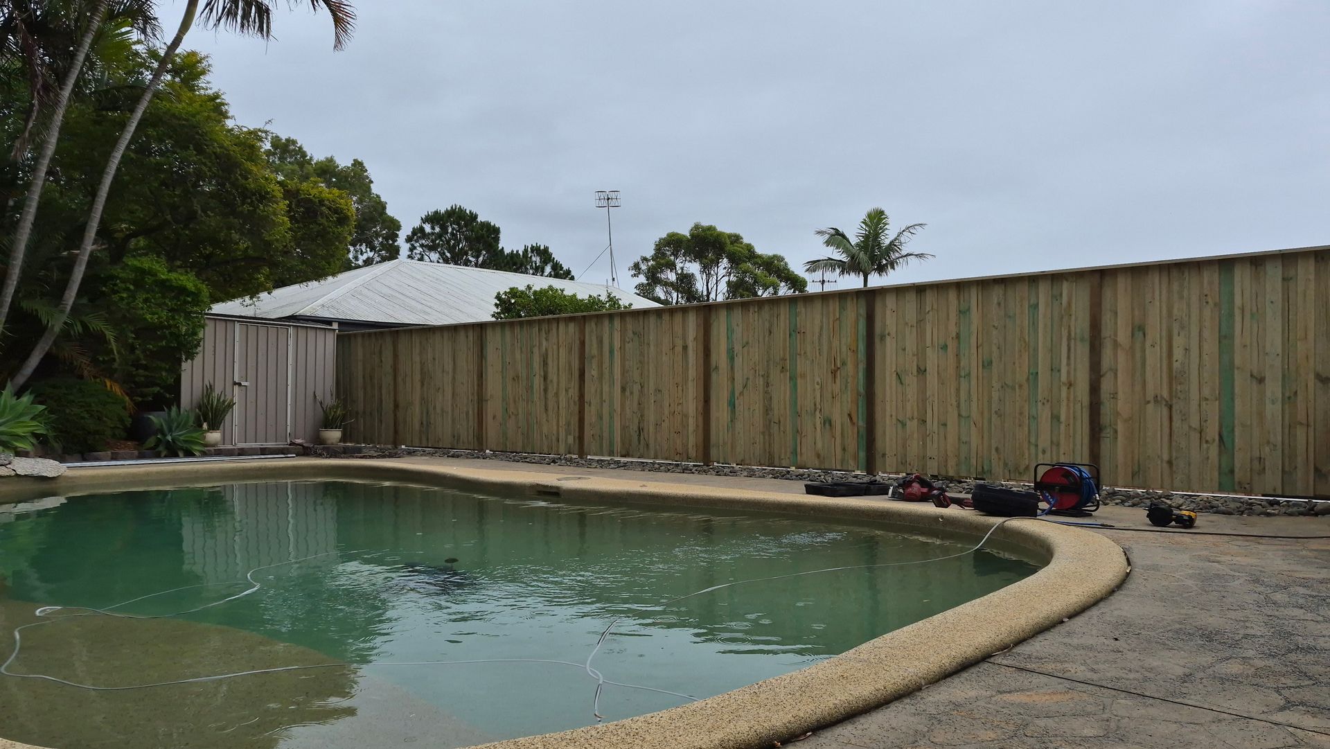 Pool surrounded by a brown fence and a cloudy sky. — Strike Fencing & Gates In Tuggerah, NSW