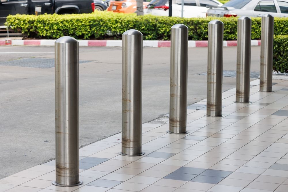 Row of silver bollards along a sidewalk, protecting a pedestrian area from vehicles. — Strike Fencing & Gates In Tuggerah, NSW