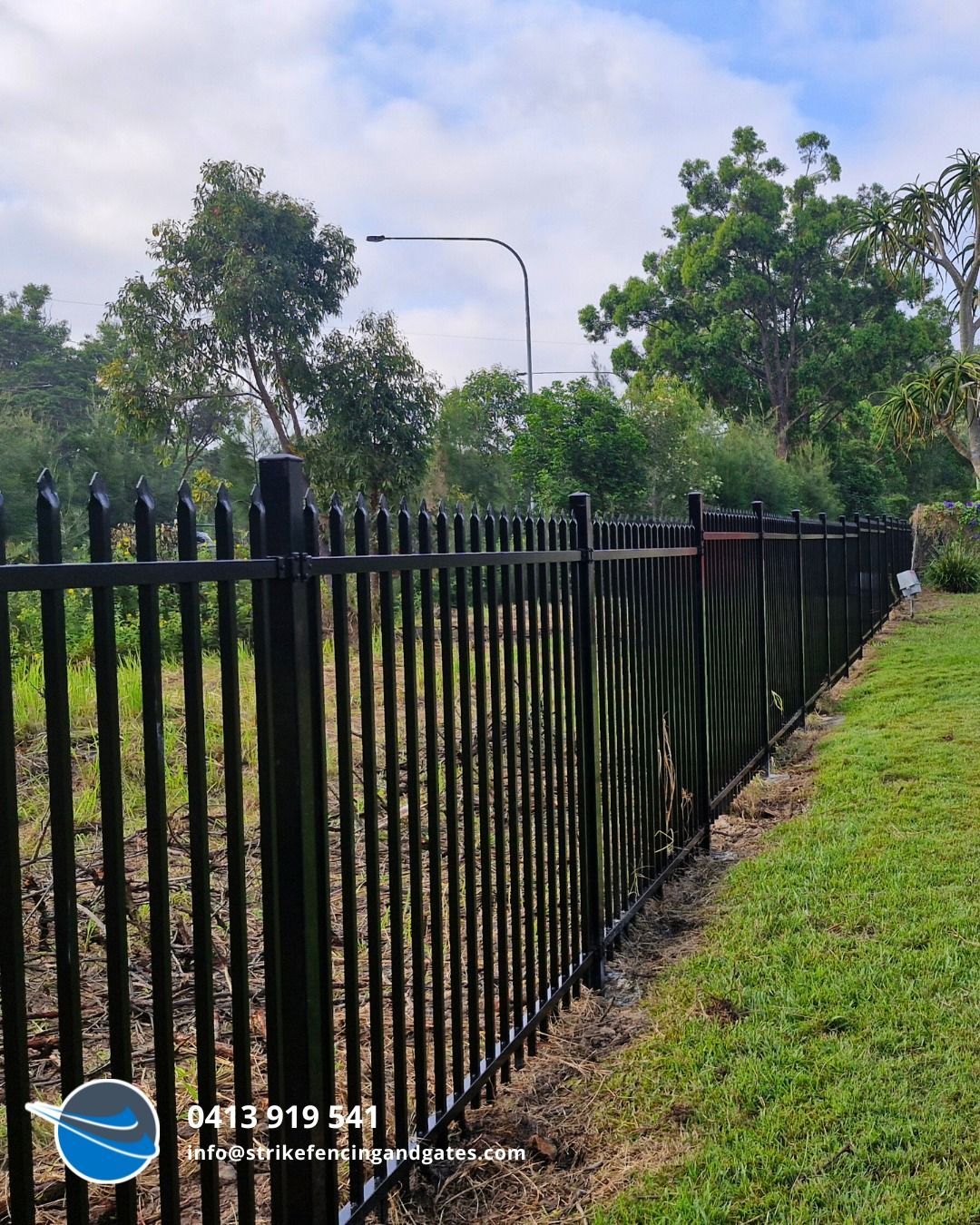Black Metal Fence Bordering a Grassy Area With Trees and a Cloudy Sky — Strike Fencing & Gates In Umina, NSW