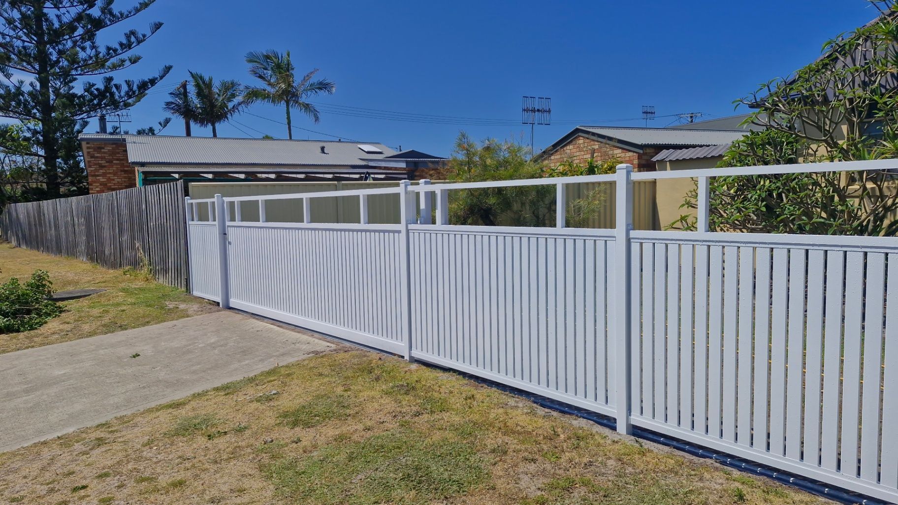 White slatted fence in front of a house, set on a sunny, blue-sky day. — Strike Fencing & Gates In Tuggerah, NSW