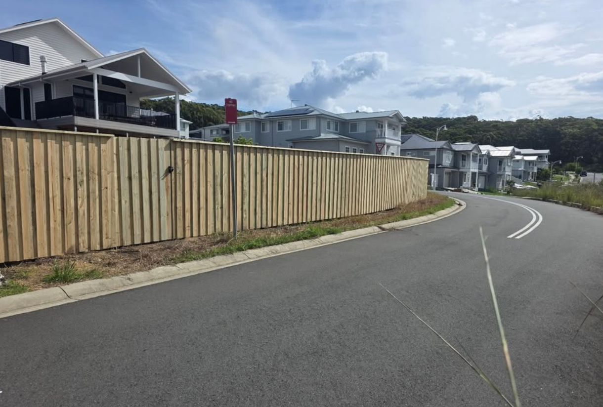 timeber fence next to a main road with a house in the background