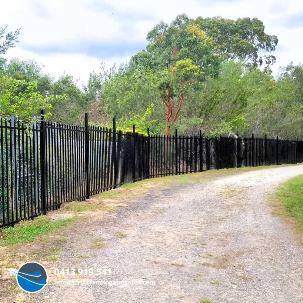 Black Metal Fence Bordering a Gravel Path — Strike Fencing & Gates In Davistown, NSW