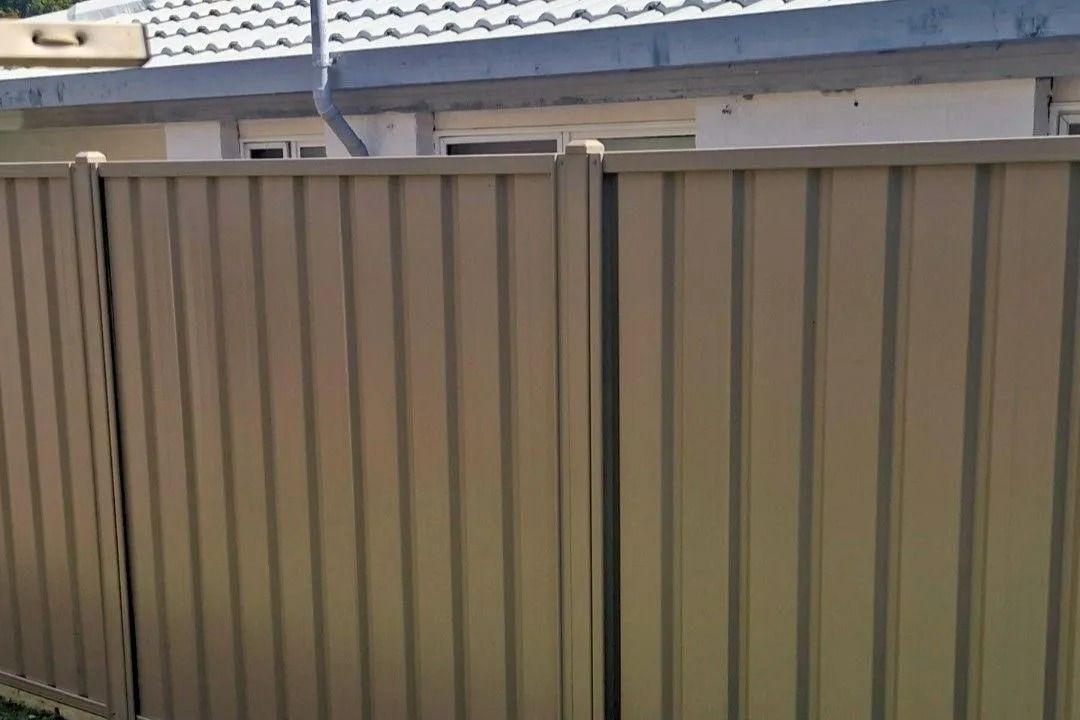Beige Corrugated Metal Fence in Front of a White Building — Strike Fencing & Gates In Tuggerah, NSW