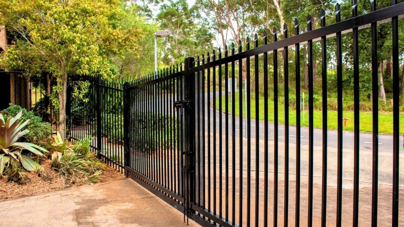 Black Metal Security Fence With Gate, Along a Sidewalk Near Foliage — Strike Fencing & Gates In Tuggerah, NSW