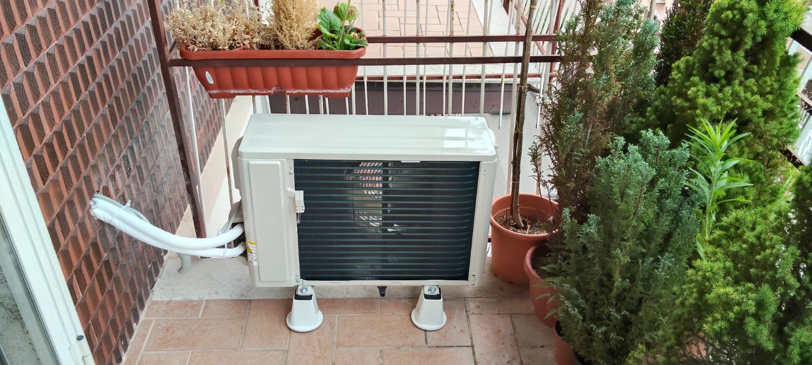 Un condizionatore è posizionato sul balcone accanto a piante in vaso.