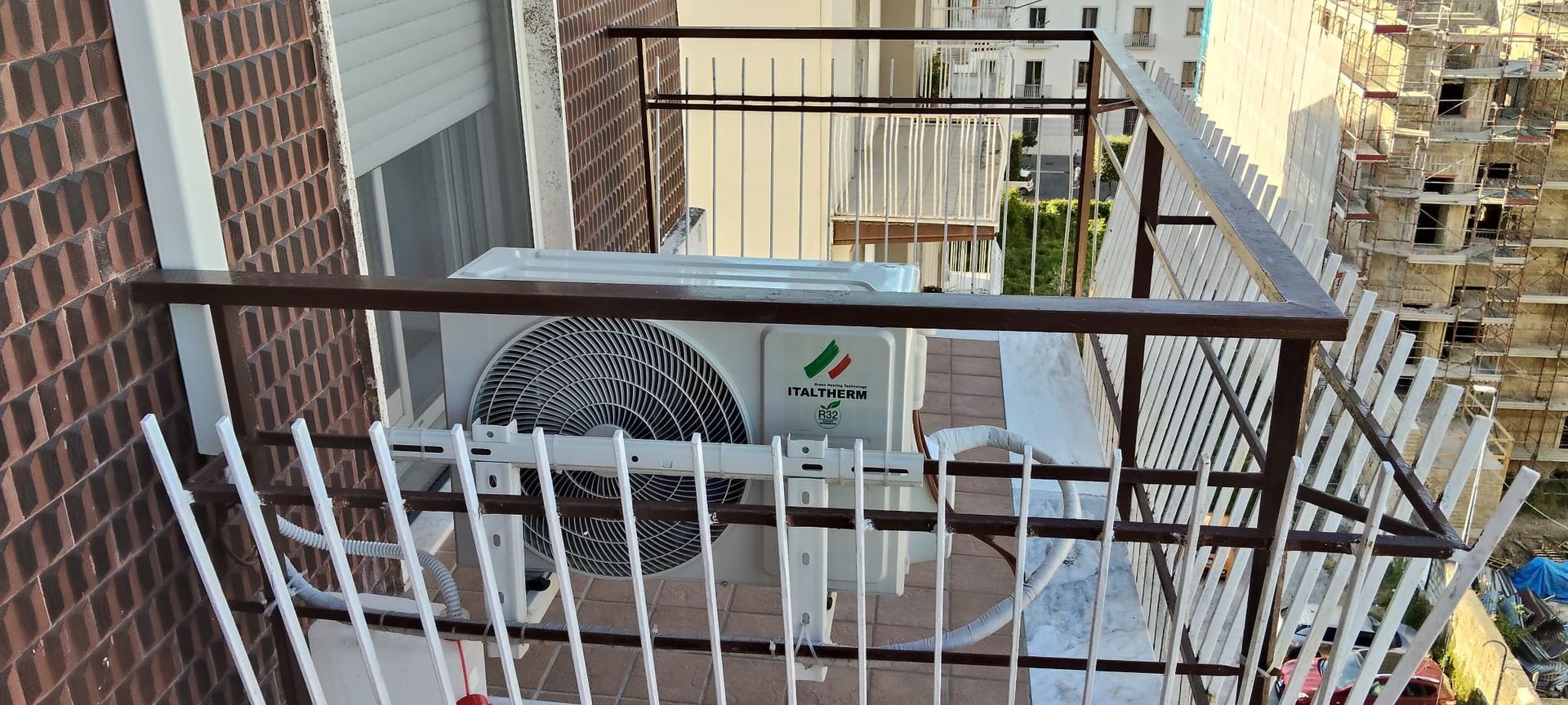 Un condizionatore è posizionato su un balcone accanto a un edificio in mattoni.