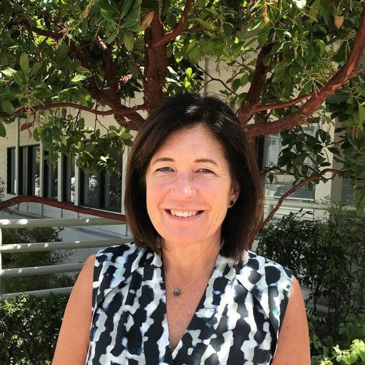 A woman in a black and white shirt is smiling in front of a tree.